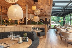 Blick in den Raum. Natürliche Materialien – heller Holzboden, Holzdecke, Sitzlounges, stimmiges Lampenkonzept.