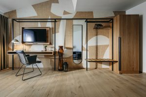 cleanes Hotelzimmer mit hochwertigem Holzboden, kunstvollen Tapetenelementen, Fernseher, Garderobe, kleinem Schreibtisch